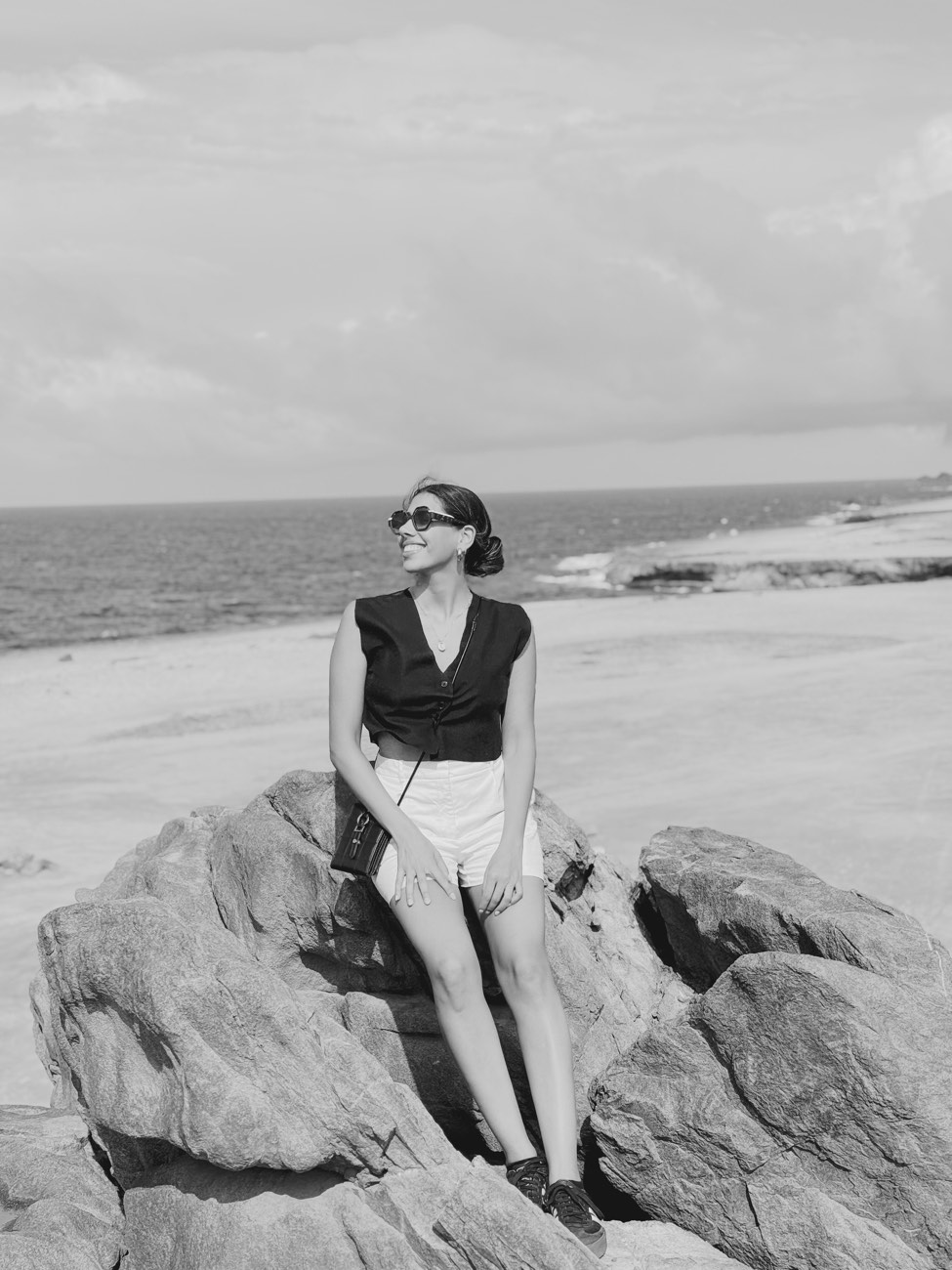 Antonia sentada en rocas frente al mar, en blanco y negro